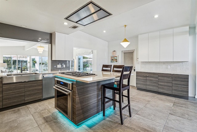 kitchen with decorative light fixtures, a center island, a kitchen breakfast bar, stainless steel appliances, and white cabinets