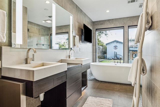 bathroom with vanity, tile walls, tile patterned floors, and a tub to relax in