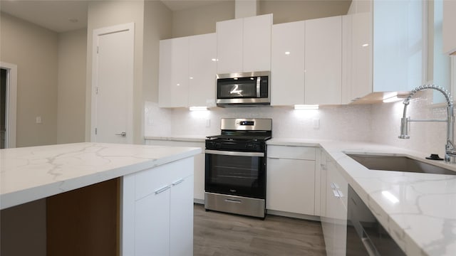 kitchen with sink, stainless steel appliances, light stone counters, white cabinets, and decorative backsplash