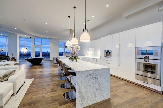 kitchen with a kitchen bar, pendant lighting, a large island, light hardwood / wood-style floors, and white cabinets