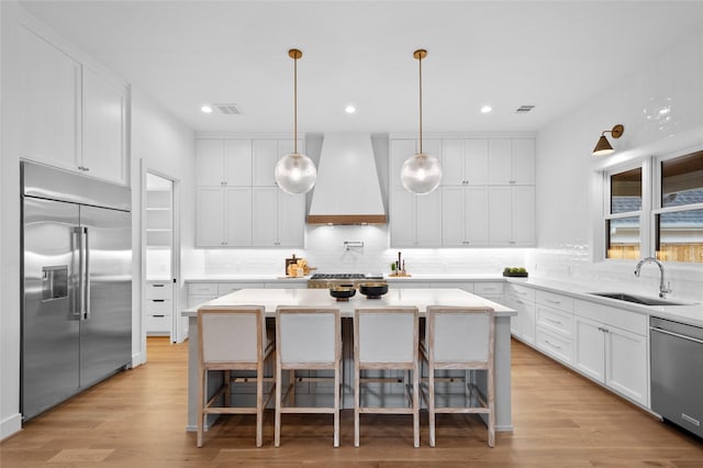 kitchen with sink, premium range hood, white cabinetry, appliances with stainless steel finishes, and a kitchen island