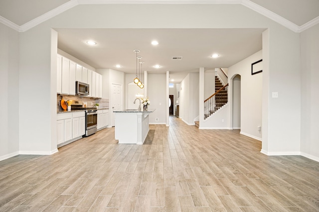 kitchen with light wood-type flooring, pendant lighting, stainless steel appliances, a kitchen island with sink, and white cabinets