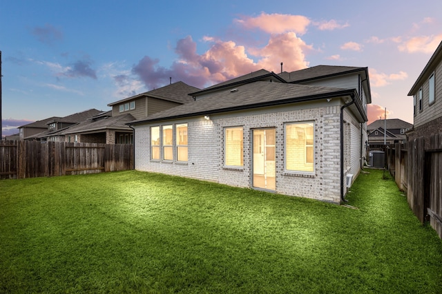 back house at dusk featuring central AC unit and a lawn