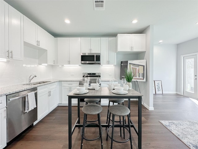 kitchen with sink, dark wood-type flooring, stainless steel appliances, light stone countertops, and white cabinets