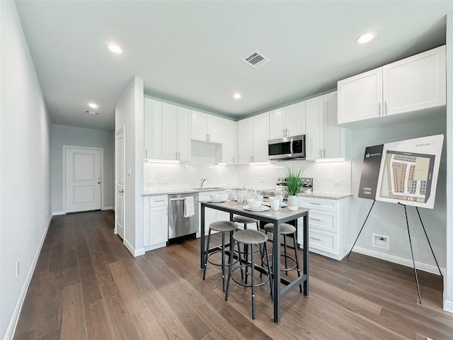 kitchen with sink, light stone counters, appliances with stainless steel finishes, dark hardwood / wood-style flooring, and white cabinets