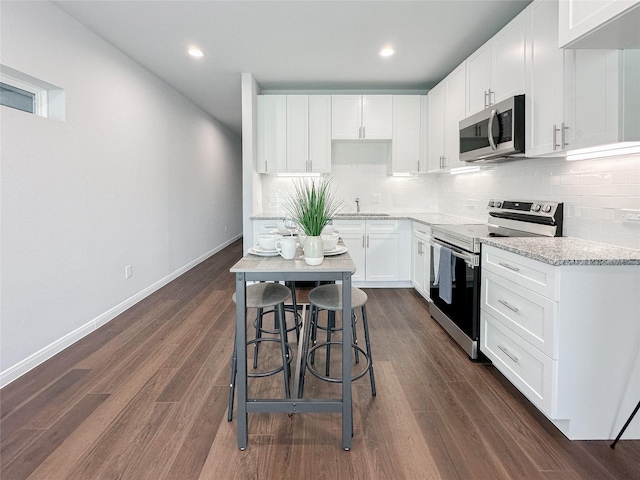 kitchen with sink, a breakfast bar area, white cabinetry, appliances with stainless steel finishes, and dark hardwood / wood-style flooring