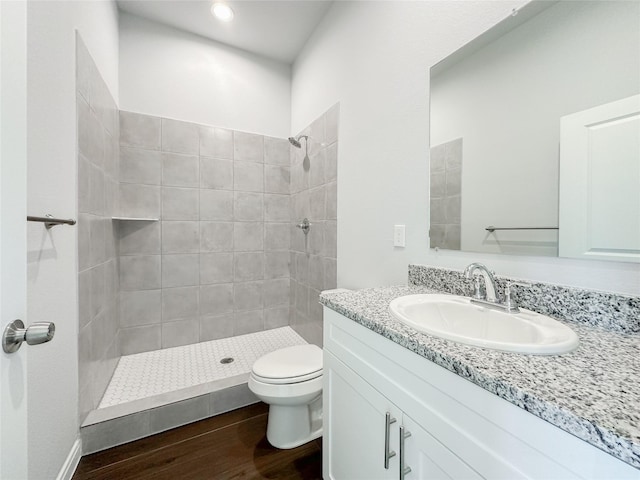 bathroom featuring wood-type flooring, toilet, vanity, and a tile shower