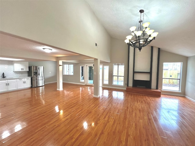 unfurnished living room with lofted ceiling, sink, a chandelier, a textured ceiling, and light wood-type flooring