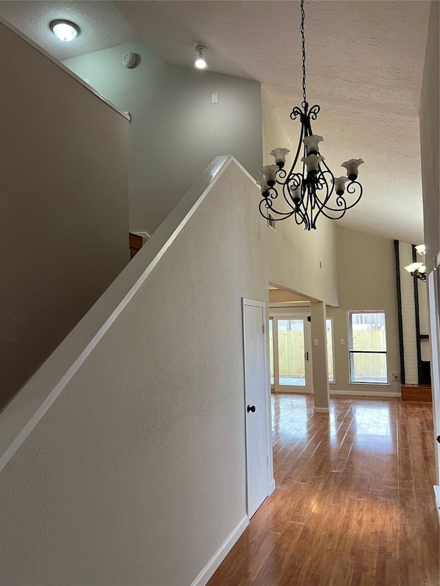 hallway with a notable chandelier, hardwood / wood-style floors, and high vaulted ceiling