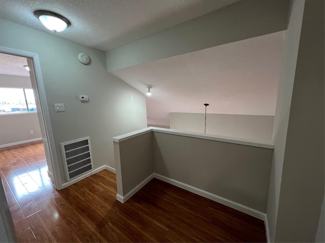 hallway with lofted ceiling, dark hardwood / wood-style floors, and a textured ceiling