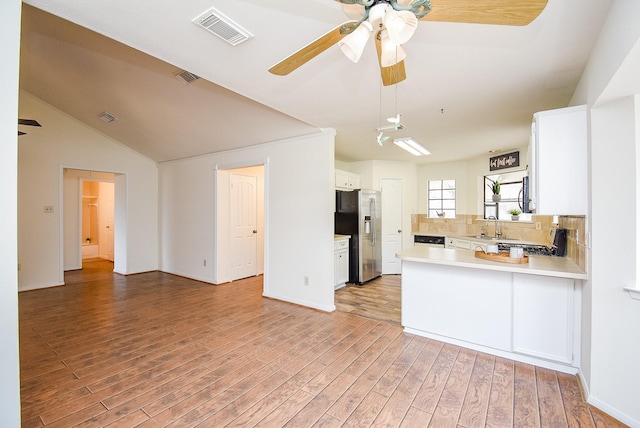 kitchen with light countertops, visible vents, white cabinets, stainless steel fridge, and a peninsula