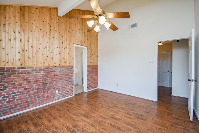 unfurnished room with high vaulted ceiling, wooden walls, dark hardwood / wood-style flooring, beamed ceiling, and brick wall