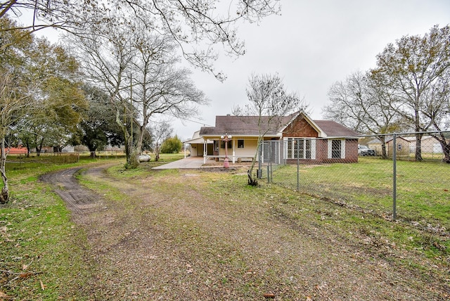 view of front of home with dirt driveway, fence, a front lawn, and brick siding