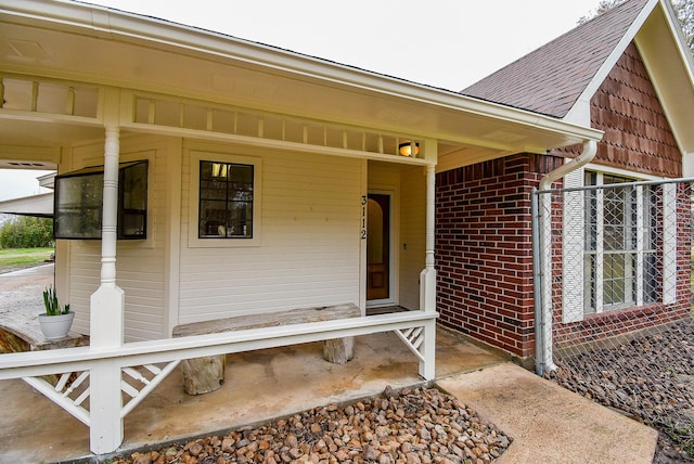 view of exterior entry with a shingled roof and brick siding