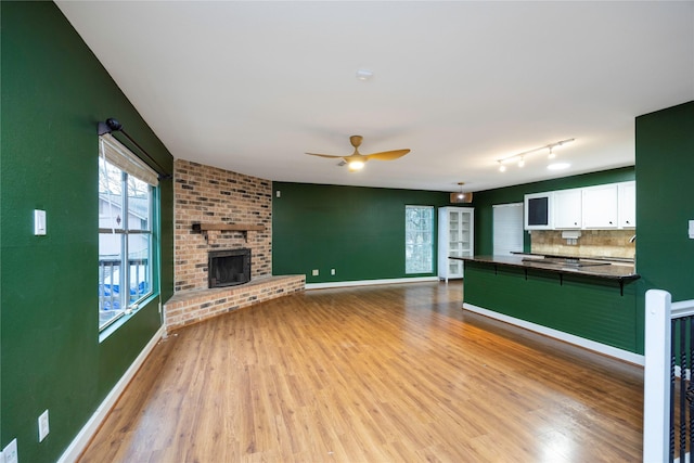 unfurnished living room featuring ceiling fan, rail lighting, a brick fireplace, and light wood-type flooring