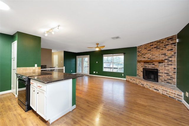 kitchen with a fireplace, white cabinets, black / electric stove, dark stone counters, and light wood-type flooring