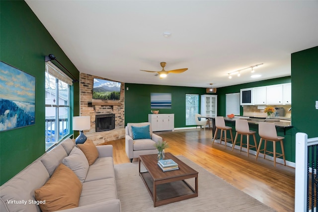 living room featuring ceiling fan, a stone fireplace, track lighting, and light hardwood / wood-style floors