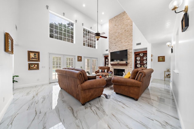 living room featuring a stone fireplace, french doors, ceiling fan, and a high ceiling