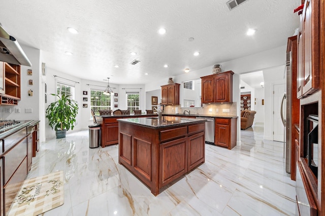 kitchen with stainless steel appliances, decorative light fixtures, an island with sink, and a textured ceiling