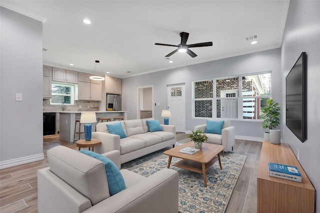 living room featuring ceiling fan, plenty of natural light, ornamental molding, and light wood-type flooring