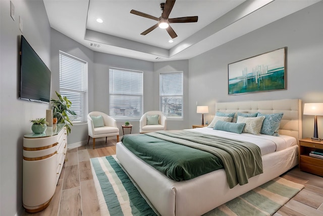 bedroom with light hardwood / wood-style floors, a raised ceiling, and ceiling fan