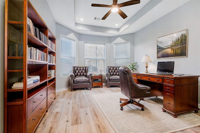 office area featuring light hardwood / wood-style flooring, ceiling fan, and a tray ceiling