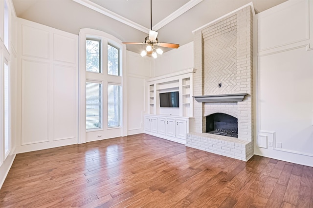 unfurnished living room with hardwood / wood-style flooring, built in features, a high ceiling, ornamental molding, and a brick fireplace