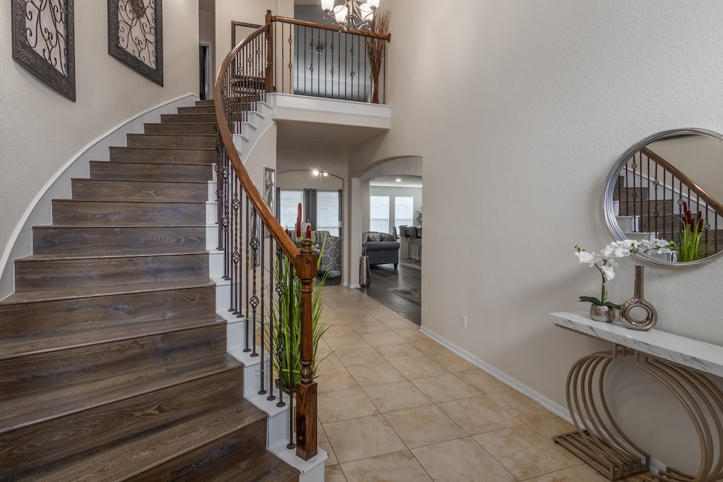 staircase with a towering ceiling, a chandelier, and tile patterned flooring