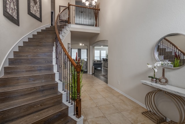 staircase with a towering ceiling, a chandelier, and tile patterned flooring