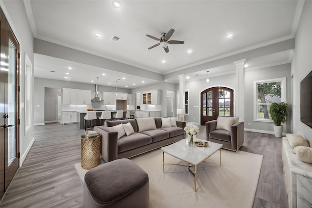 living room featuring french doors, crown molding, light wood-type flooring, ceiling fan, and decorative columns