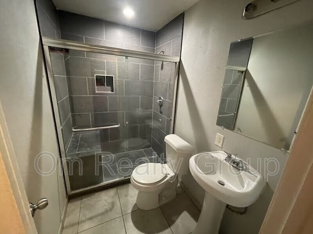 bathroom with tile patterned floors, toilet, a shower with shower door, and sink