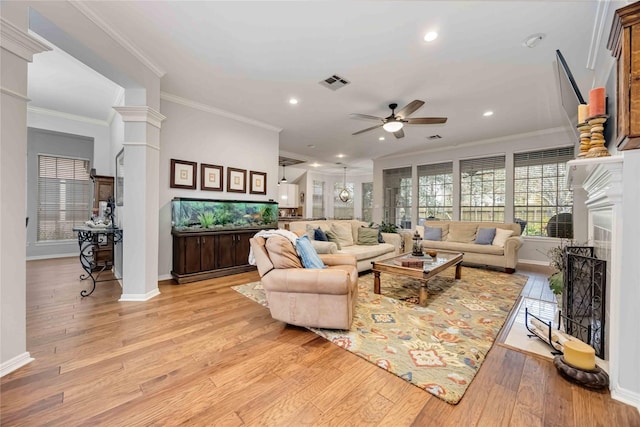 living room with ornate columns, ornamental molding, ceiling fan, and light wood-type flooring