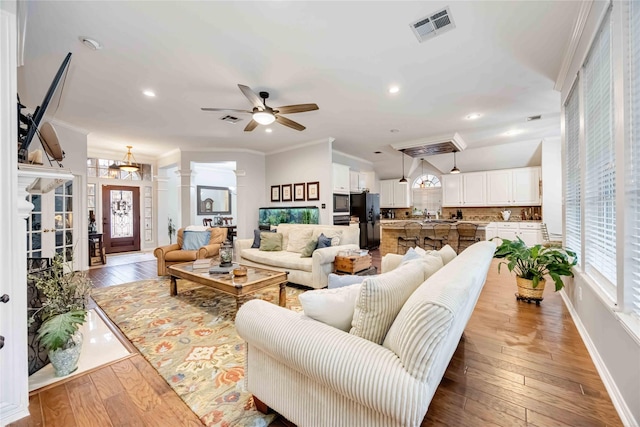 living room featuring decorative columns, wood-type flooring, ceiling fan, and crown molding