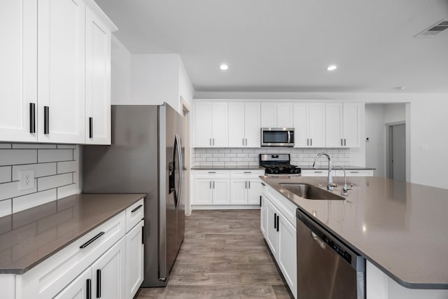 kitchen with sink, tasteful backsplash, appliances with stainless steel finishes, an island with sink, and white cabinets