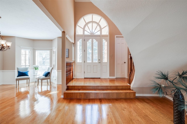 foyer entrance with a high ceiling, a textured ceiling, a notable chandelier, and light hardwood / wood-style floors