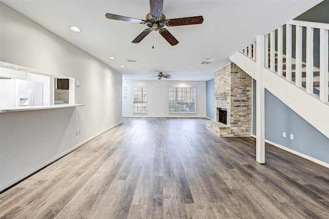 unfurnished living room with wood-type flooring, a large fireplace, and ceiling fan