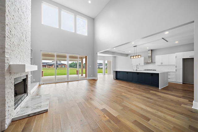 unfurnished living room featuring sink, a towering ceiling, a stone fireplace, and light hardwood / wood-style floors