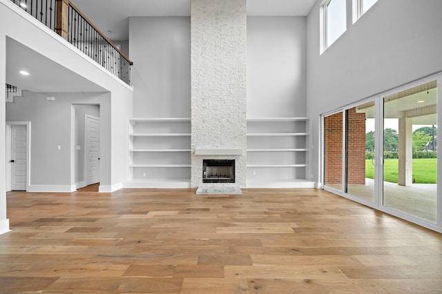 unfurnished living room featuring a high ceiling, a stone fireplace, built in features, and light hardwood / wood-style flooring