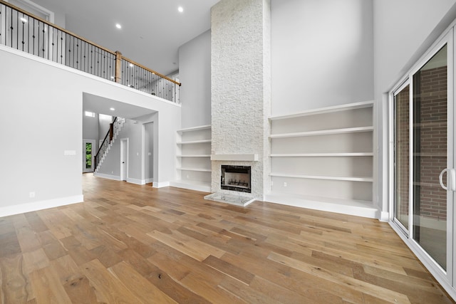 unfurnished living room with built in shelves, a towering ceiling, a fireplace, and light hardwood / wood-style floors