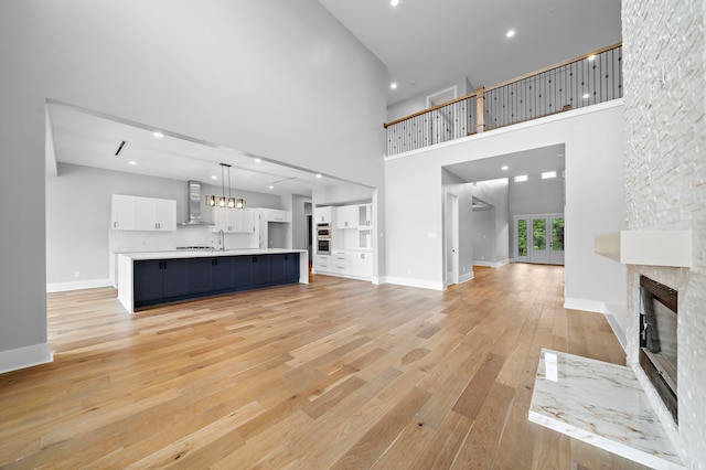 unfurnished living room featuring light hardwood / wood-style flooring, sink, a towering ceiling, and a stone fireplace