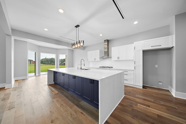 kitchen featuring tasteful backsplash, wall chimney range hood, a large island with sink, and white cabinets