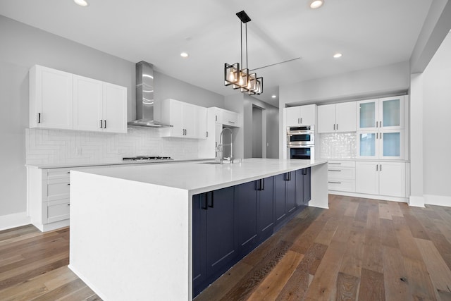 kitchen with a large island, sink, tasteful backsplash, white cabinets, and wall chimney exhaust hood