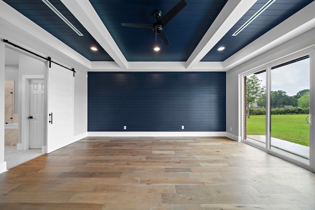 empty room featuring beam ceiling, ceiling fan, a barn door, and light wood-type flooring