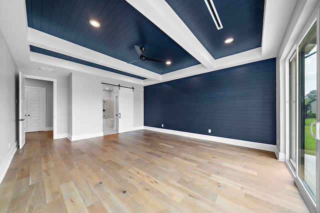 empty room with a barn door, a healthy amount of sunlight, ceiling fan, and light hardwood / wood-style floors