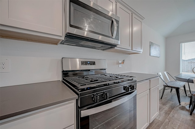 kitchen with white cabinetry, gas range, light hardwood / wood-style floors, and lofted ceiling