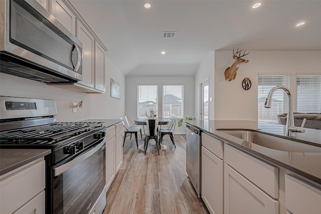 kitchen with vaulted ceiling, appliances with stainless steel finishes, sink, white cabinets, and light hardwood / wood-style flooring