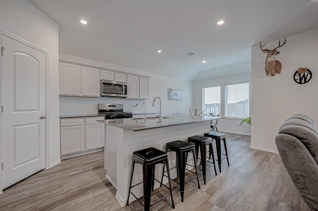 kitchen with sink, a breakfast bar area, light wood-type flooring, appliances with stainless steel finishes, and an island with sink