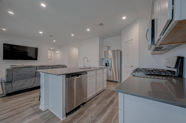 kitchen featuring sink, light hardwood / wood-style flooring, stainless steel appliances, white cabinets, and a center island with sink