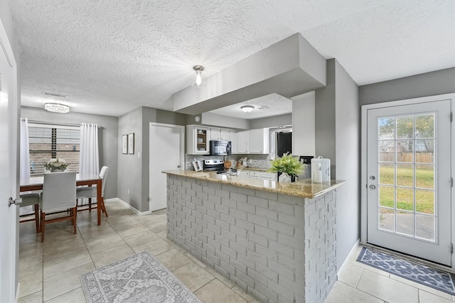 kitchen with black microwave, a peninsula, white cabinets, electric stove, and light stone countertops