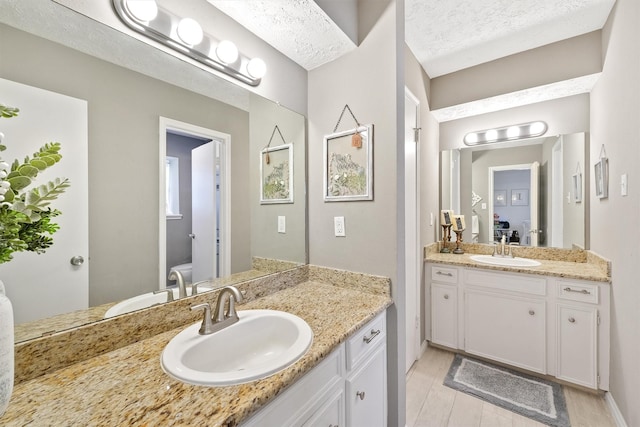 bathroom featuring two vanities, a sink, a textured ceiling, and toilet